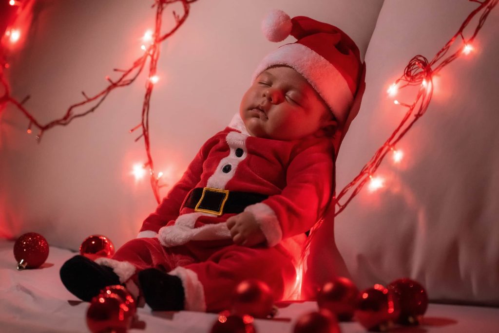 neonato vestito da babbo natale dorme sul letto con led rossi accesi