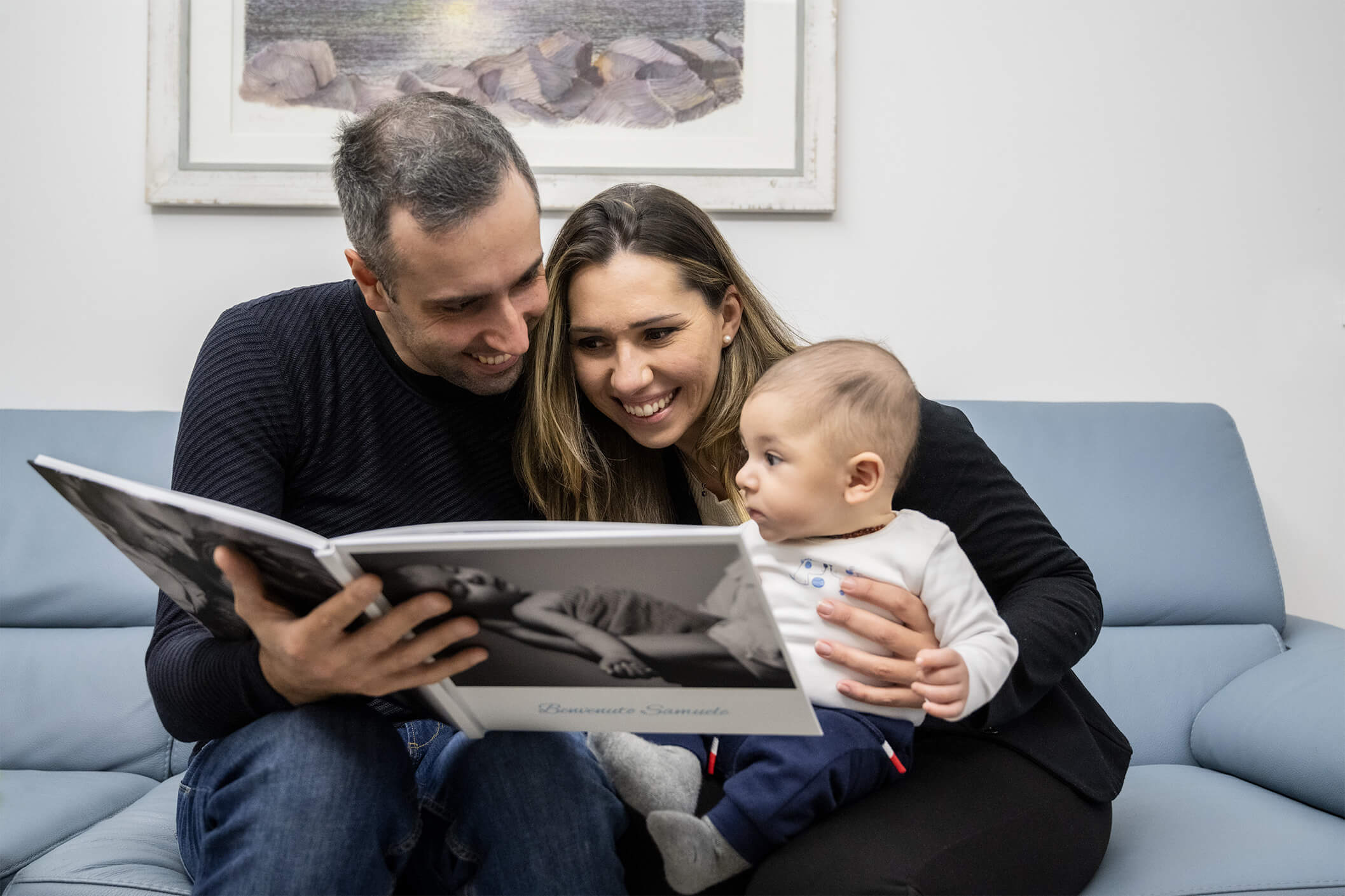 genitori sorridenti con bambino in braccio guardano il fotolibro servizio fotografico maternity milano monza